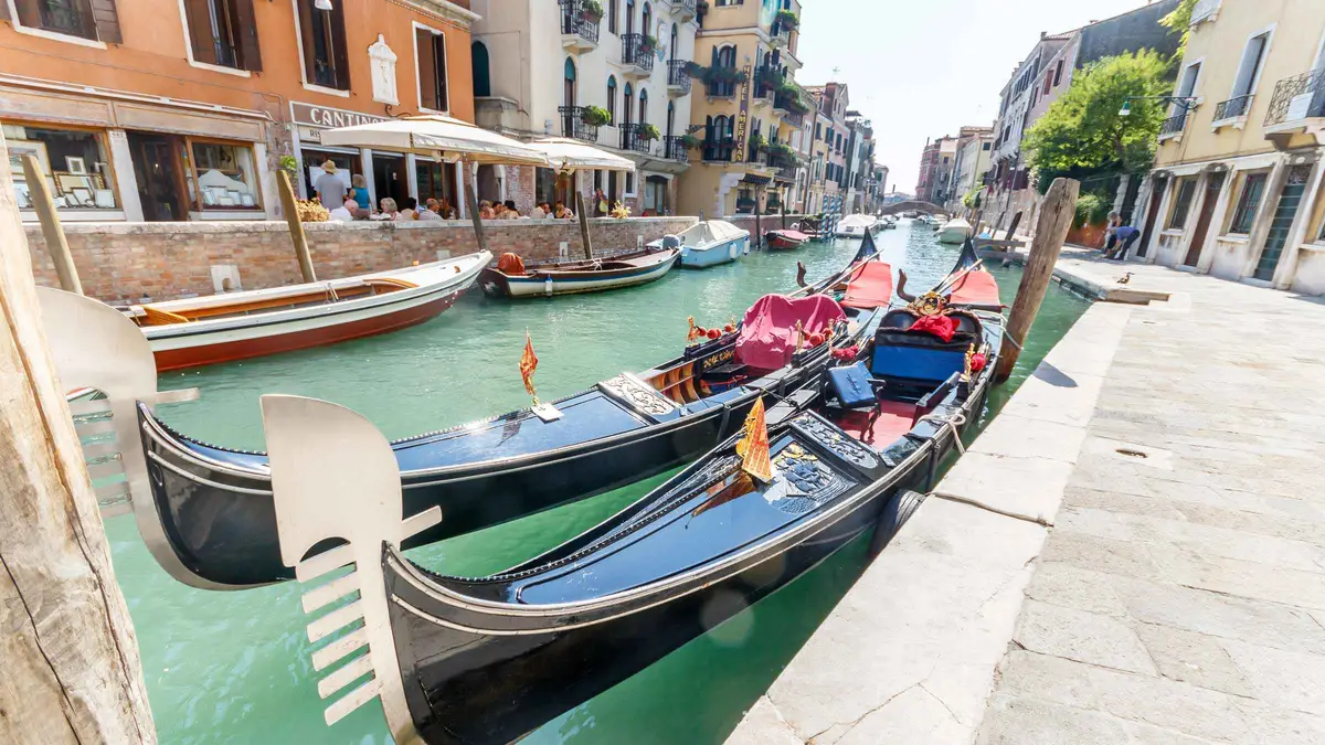 Traditional black gondola with five seated passengers turning into a narrow side canal on a shared gondola ride in Venice, Italy